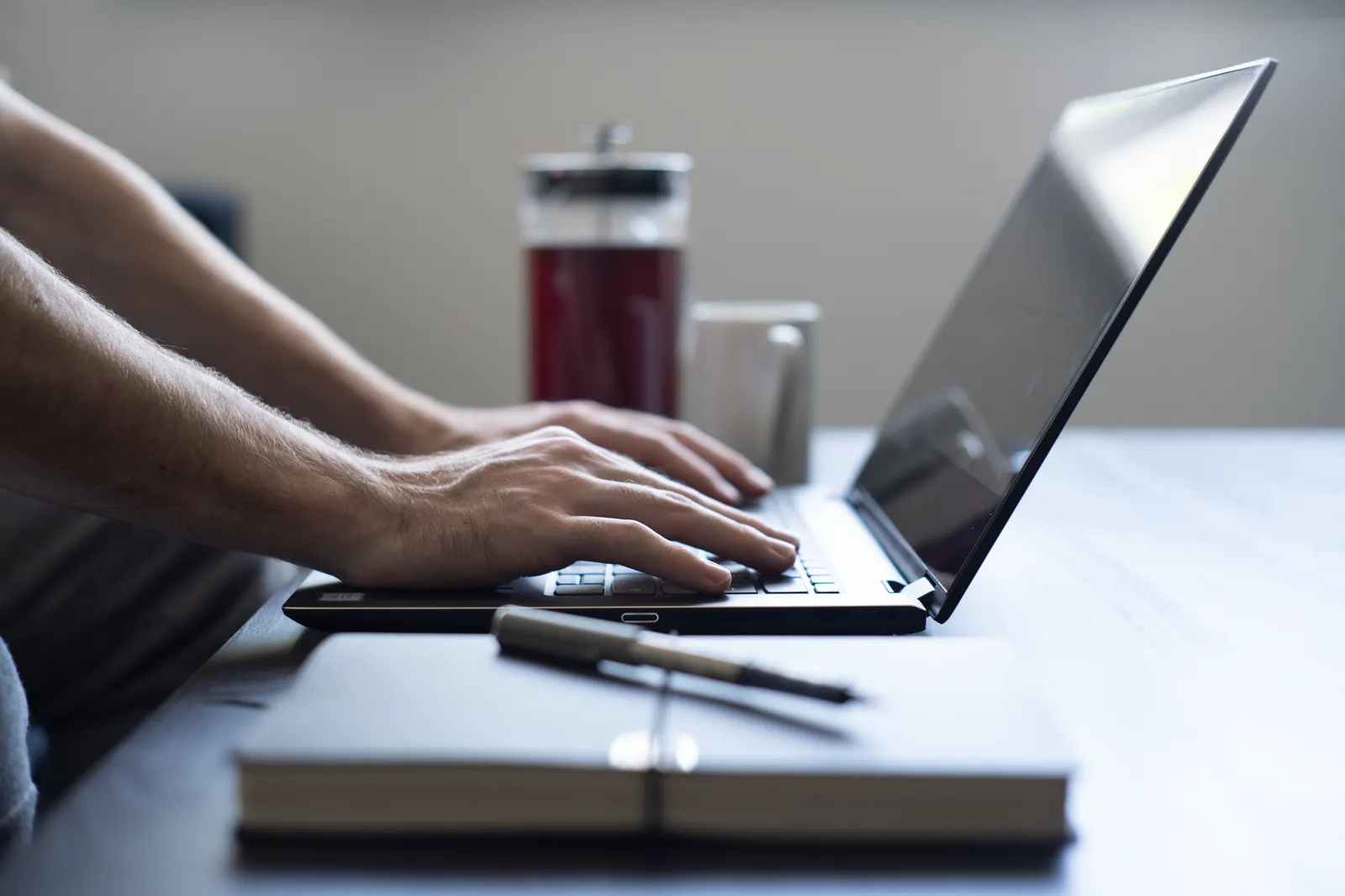 Mãos digitando em um notebook ao lado de um caderno, como o dono que trabalha para a empresa aparecer no Google de graça