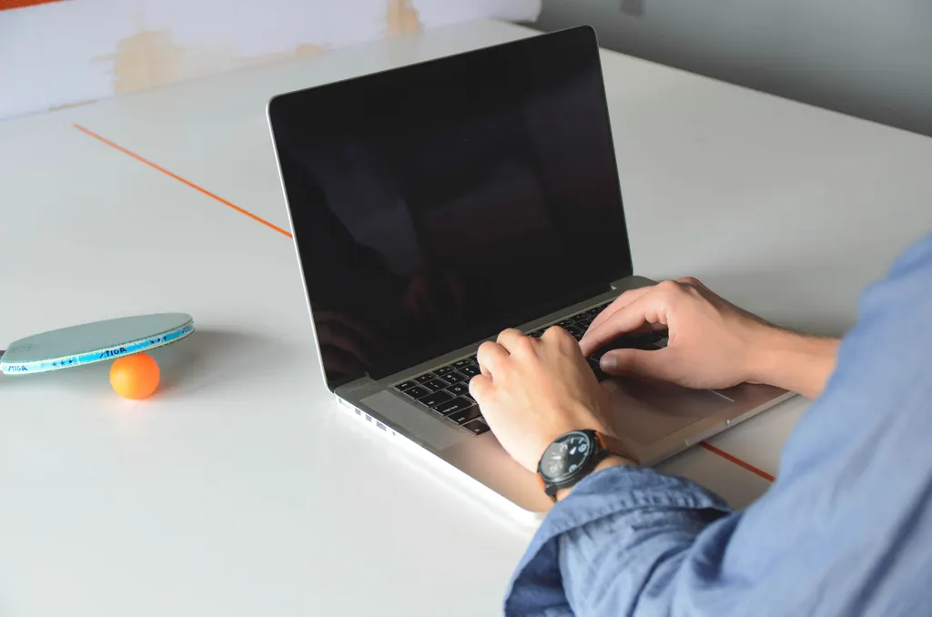 Mãos digitando num notebook sobre a mesa, como o dono que escreve as perguntas frequentes da base de conhecimento para chatbot