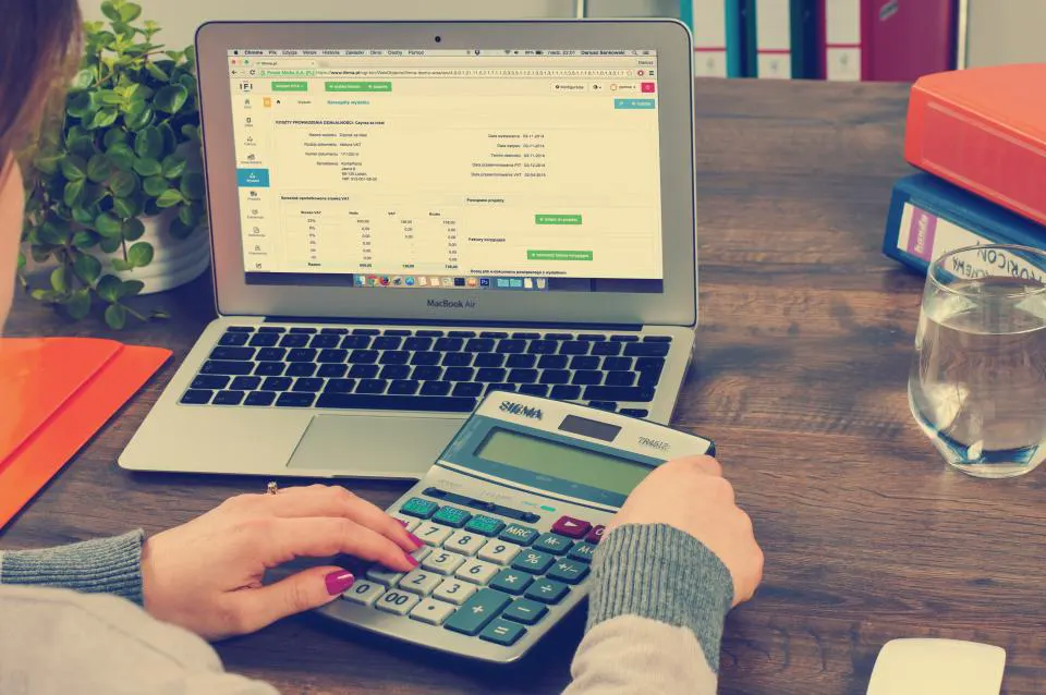 Mãos fazendo contas numa calculadora ao lado do notebook, como quem vai calcular preço de venda com cuidado