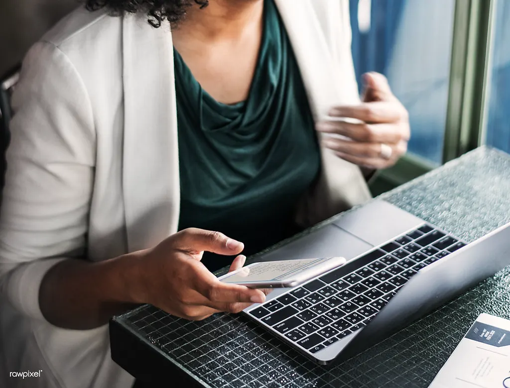 Mulher segurando o celular ao lado do notebook, planejando as publicações do canal do WhatsApp da empresa