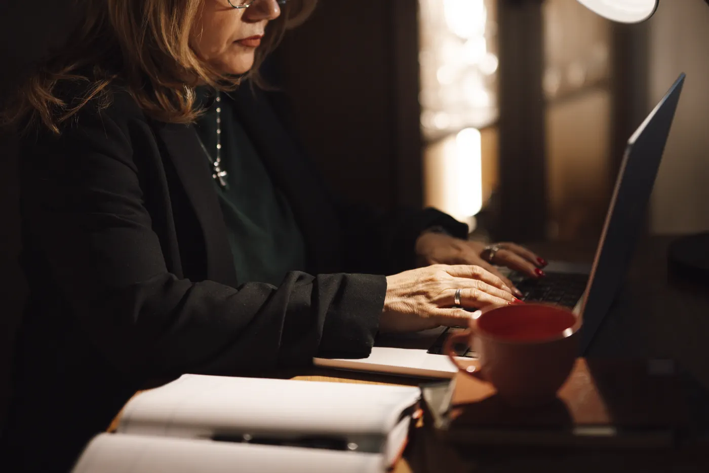 Empresária digitando no notebook à noite com um caderno aberto ao lado, montando uma apresentação com IA