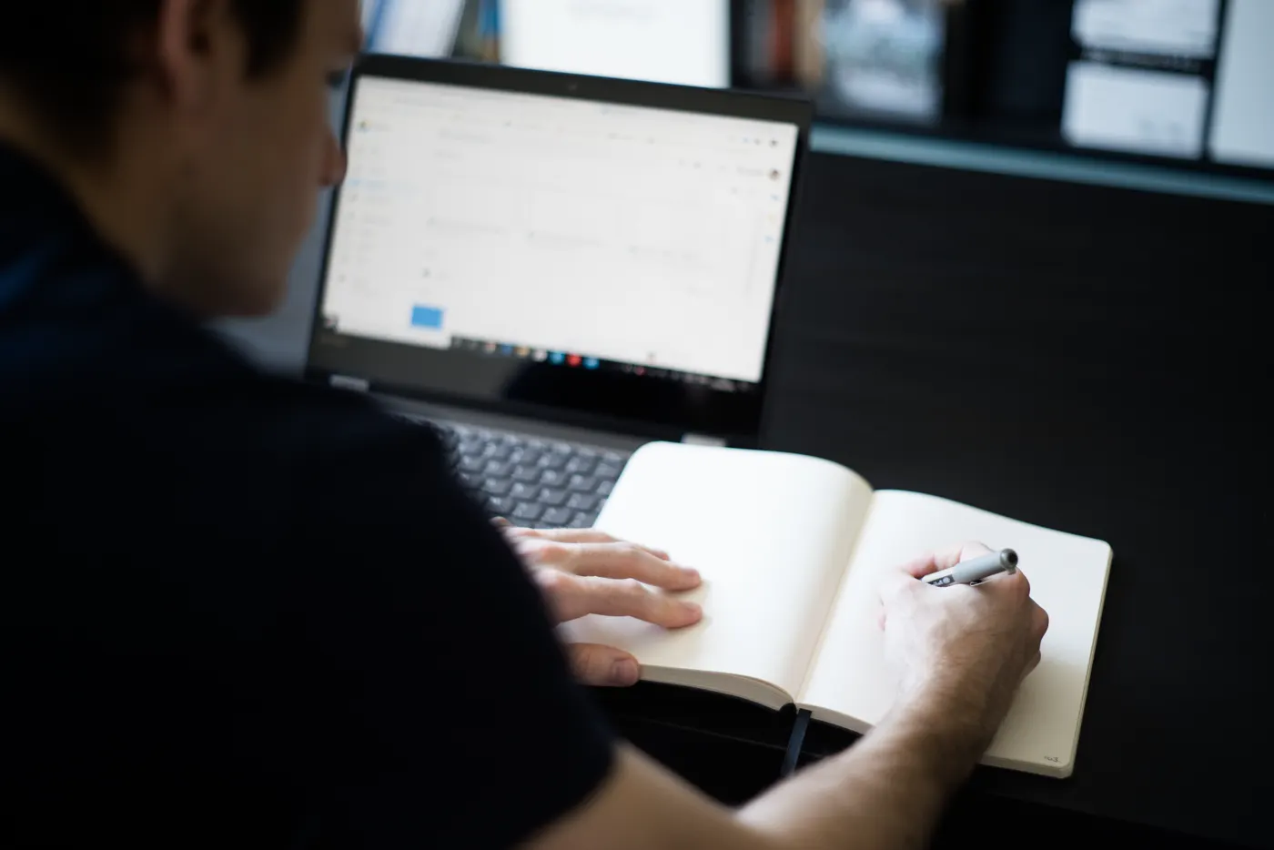 Homem fazendo anotações em um caderno ao lado do notebook, revisando o conteúdo de uma apresentação