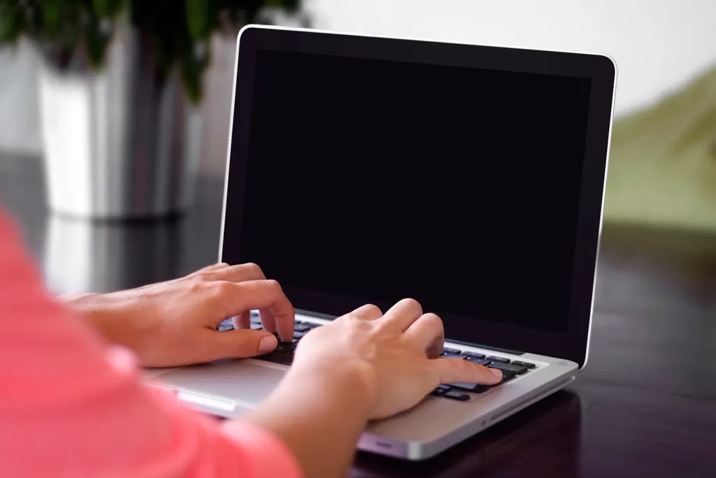 Mãos digitando no notebook sobre uma mesa escura, testando a busca do ChatGPT pelo serviço da empresa