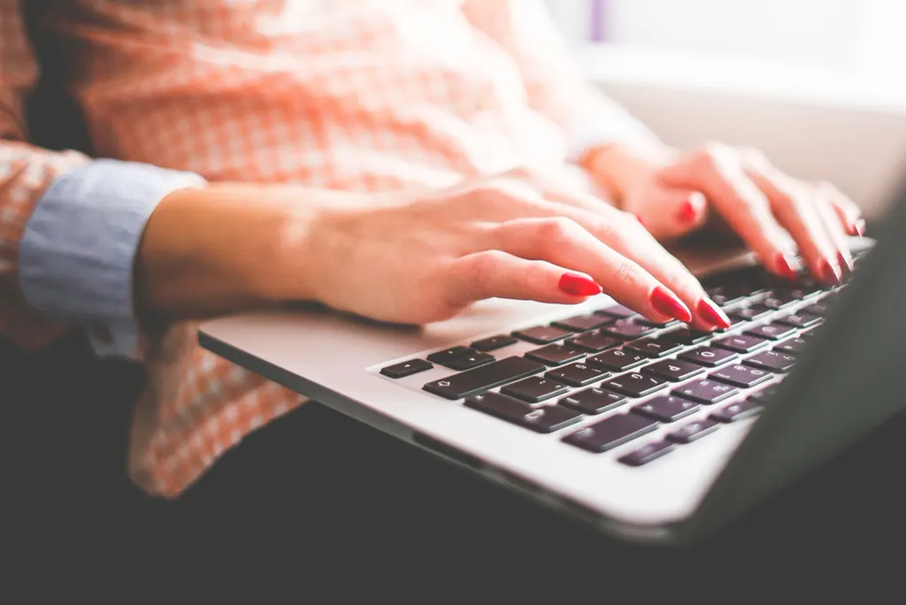 Mãos de uma mulher digitando no notebook, testando no dia a dia como começar a usar IA na empresa