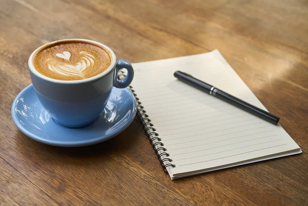 Caderno aberto e caneta ao lado de uma xícara de café, pronto para escrever o modelo de POP da equipe