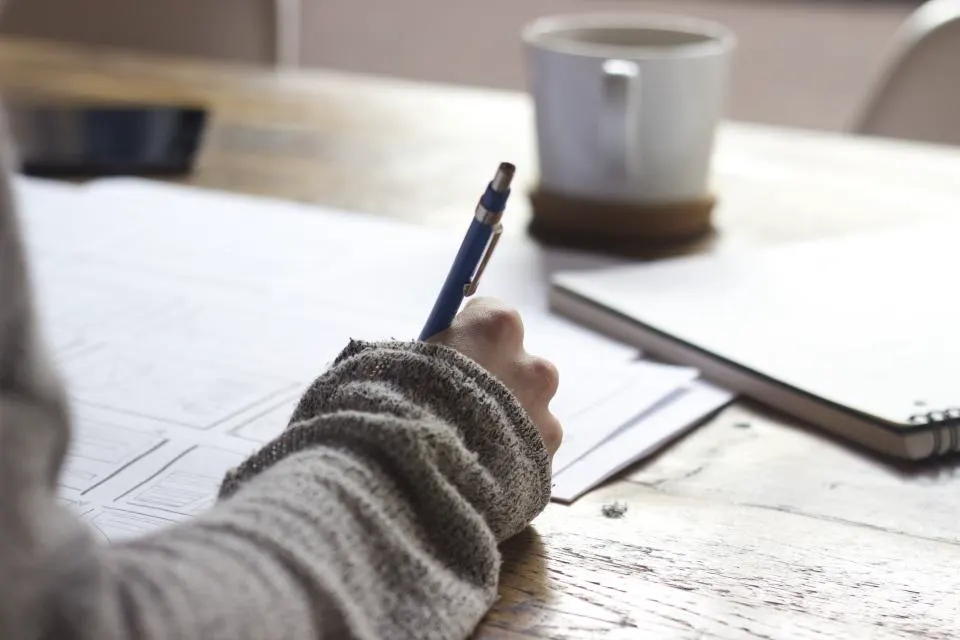 Pessoa escrevendo à mão em folhas sobre a mesa, aprendendo como fazer um POP para a empresa