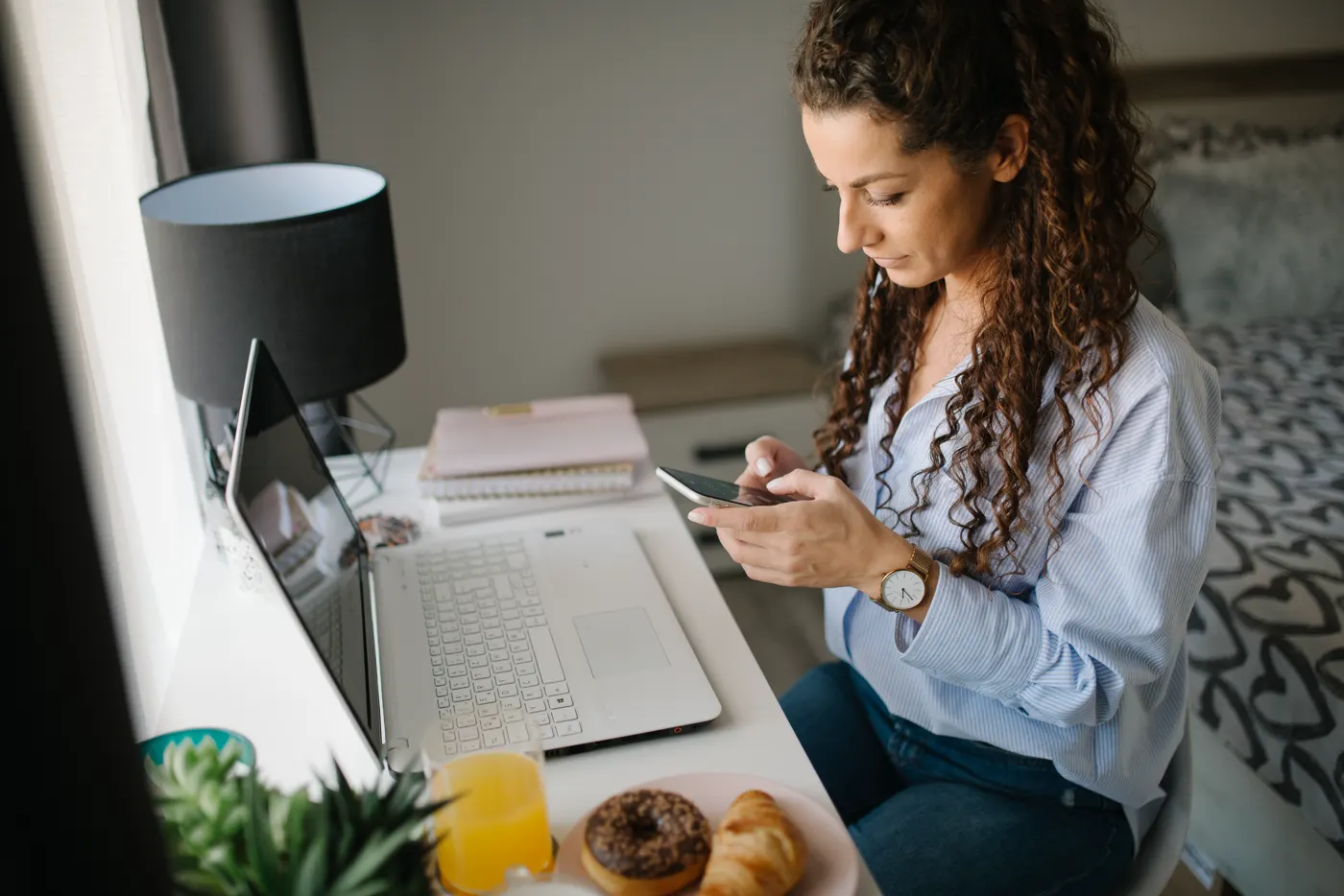 Empreendedora usando o celular ao lado do notebook, cuidando dos canais que ajudam a parar de depender de indicação