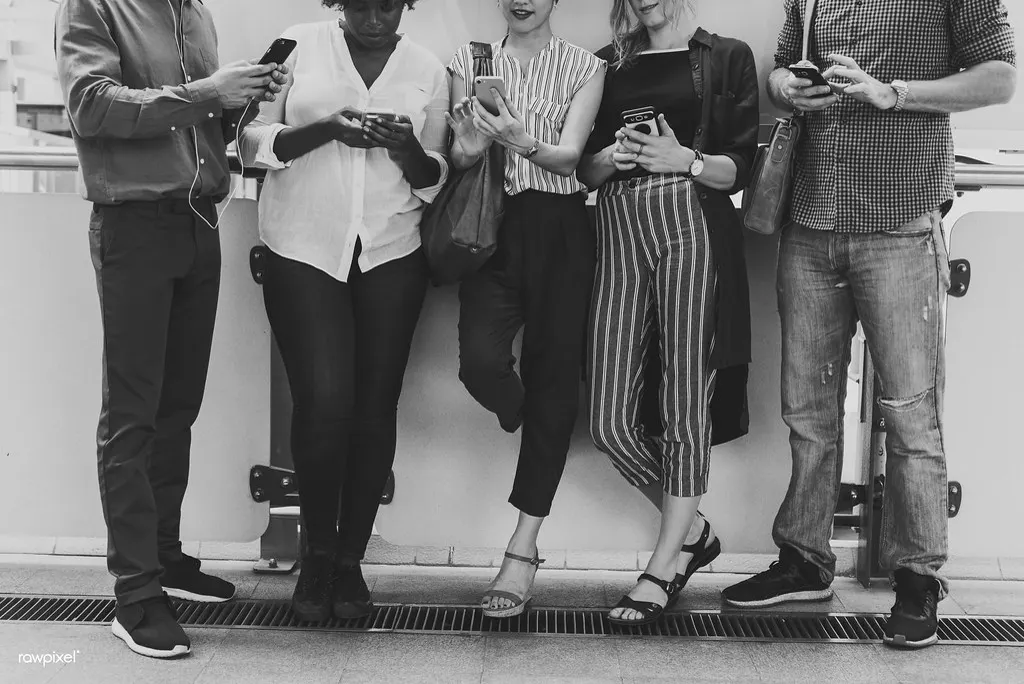 Grupo de cinco pessoas encostadas na parede olhando o celular, ilustrando os dados de redes sociais em 2026