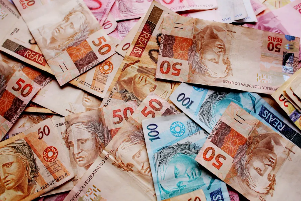 Cédulas de 50 e 100 reais espalhadas, lembrando o impacto do IBS e CBS no caixa da pequena empresa