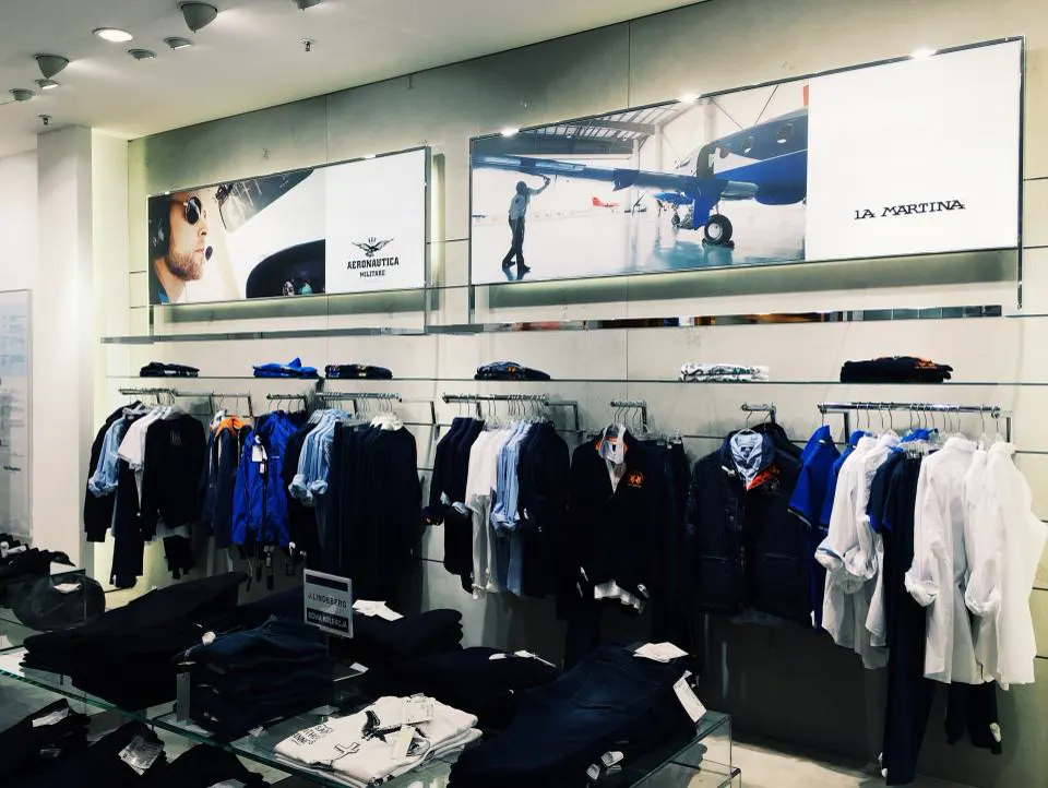 Loja de roupas com araras organizadas e peças dobradas no balcão de vidro, exemplo de exposição que ajuda a vender mais na loja