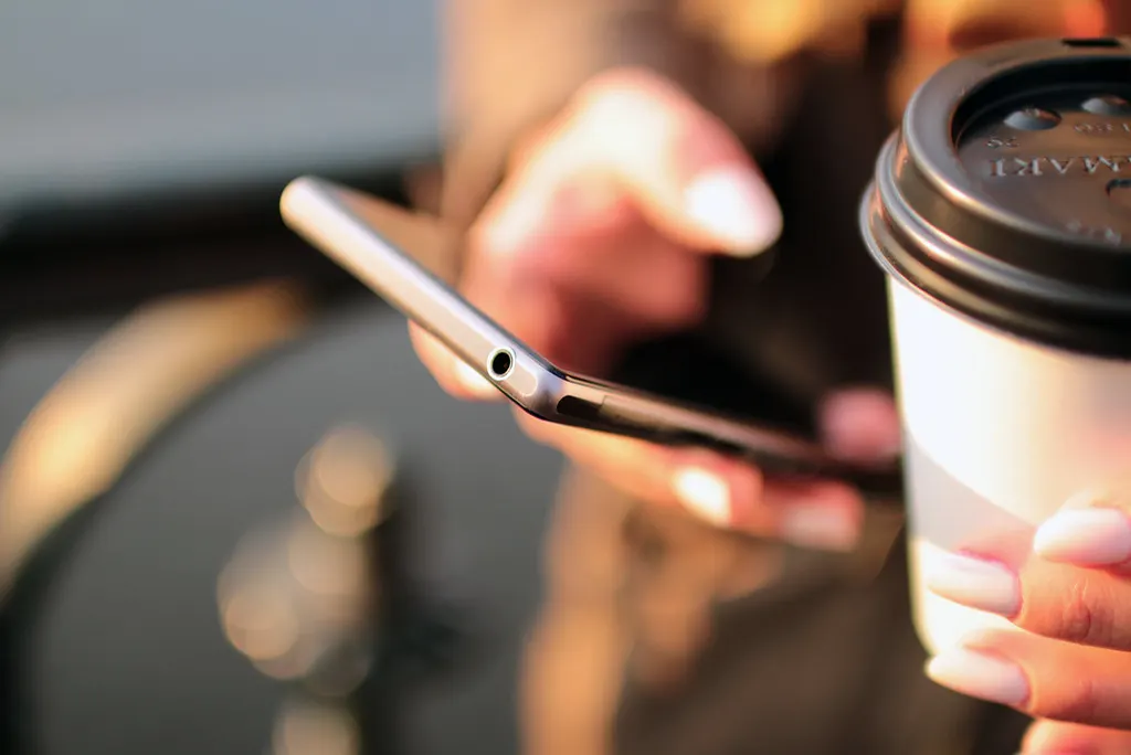Pessoa segurando um copo de café e mexendo no celular, como o cliente atendido pela IA no WhatsApp enquanto o Meta Muse para empresas não chega ao Brasil