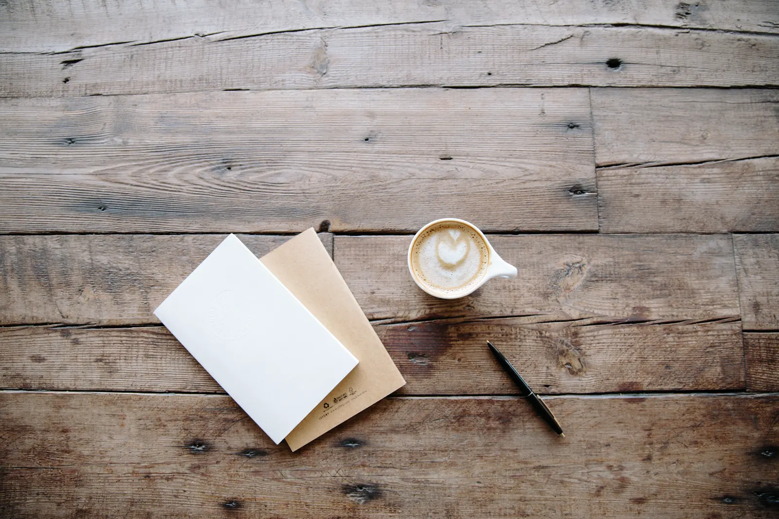 Cadernos, caneta e café sobre uma mesa de madeira, prontos para o planejamento anual da empresa