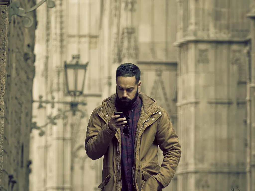 Homem olhando o celular na rua enquanto recebe mensagens configuradas com os recursos do WhatsApp Business