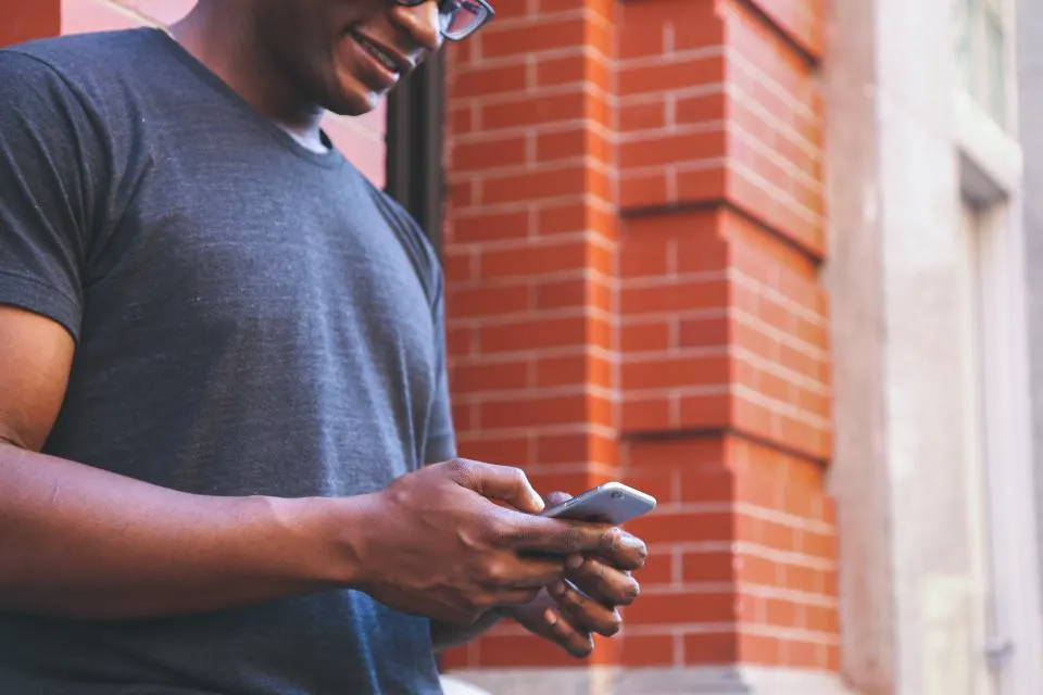 Homem sorrindo enquanto olha o celular na rua, como o cliente que procura uma empresa no Google Maps