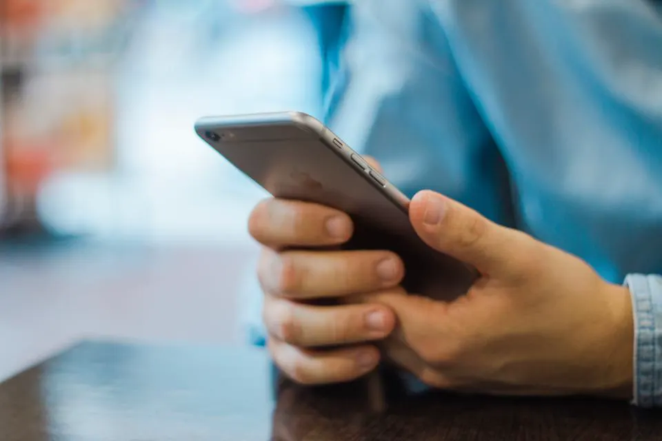 Mão segurando um celular sobre a mesa, como o dono que revisa as regras do Perfil da Empresa no Google