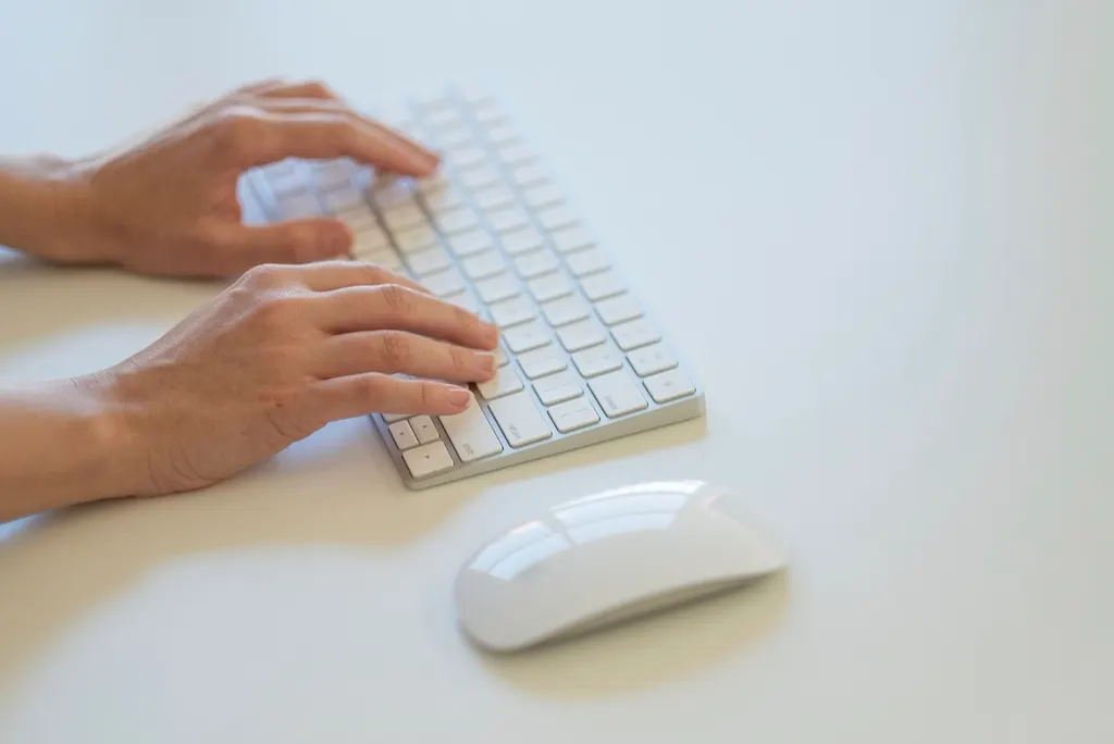 Mãos digitando em teclado branco, ajustando a automação de processos de uma pequena empresa